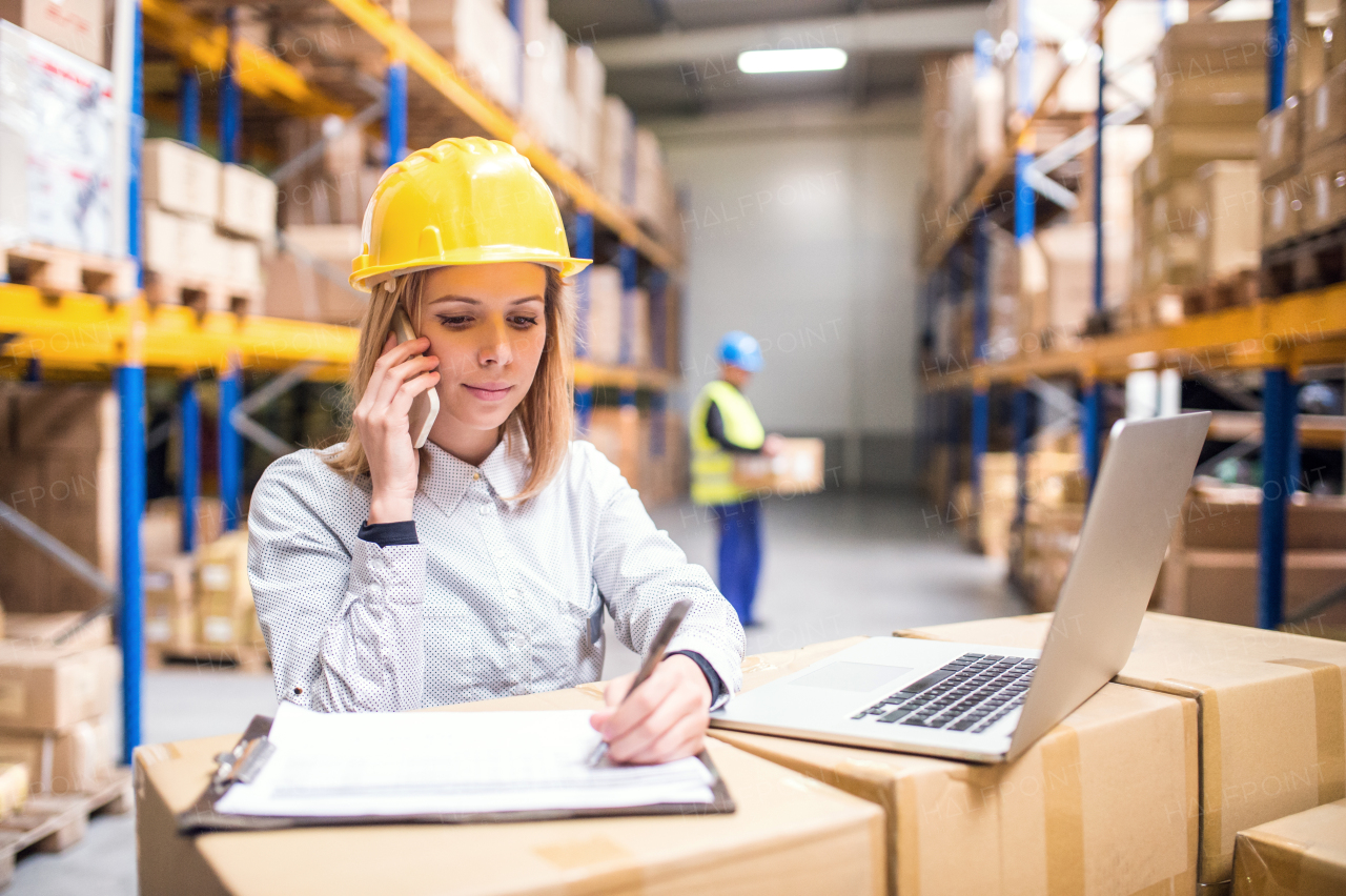 Young workers with laptop and smartphone, working together in a warehouse.