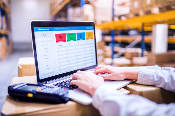 Unrecognizable young woman warehouse worker or supervisor working on a laptop.