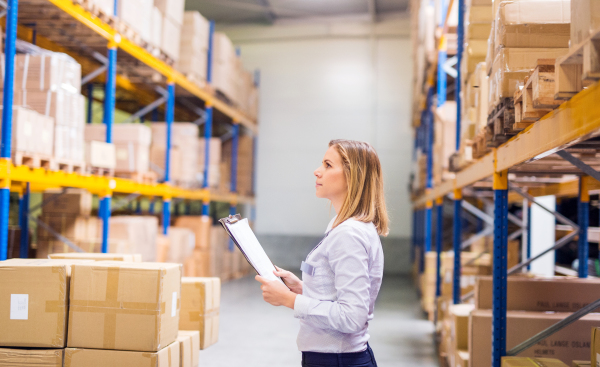 Young woman warehouse worker or supervisor with clipboard, controlling stock.