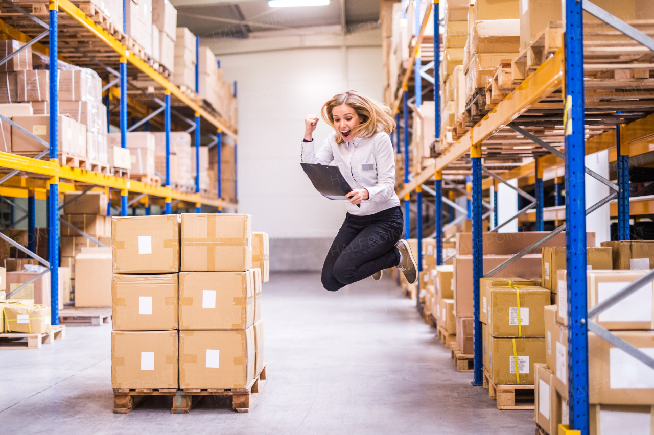 Overjoyed young female worker or supervisor in a warehouse. Happy woman jumping and feeling ecstatic. Sincere emotions.