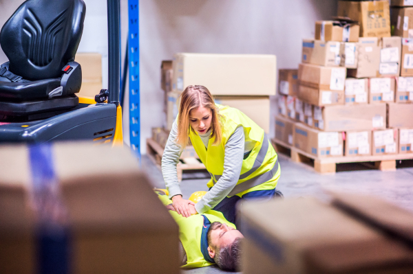 An accident in a warehouse. Woman performing cardiopulmonary resuscitation. Man lying on the floor.