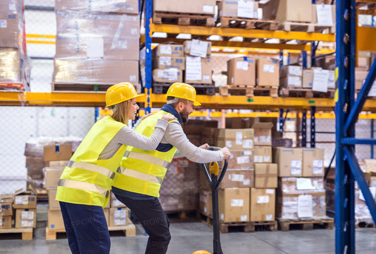 Two young workers in a warehouse, having a ride on a pallet truck.