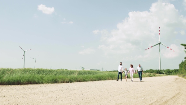 A front view of multigeneration family walking on field on wind farm.