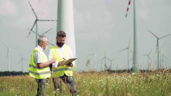 Two engineers or technicians with clipboard standing on wind farm, making notes.