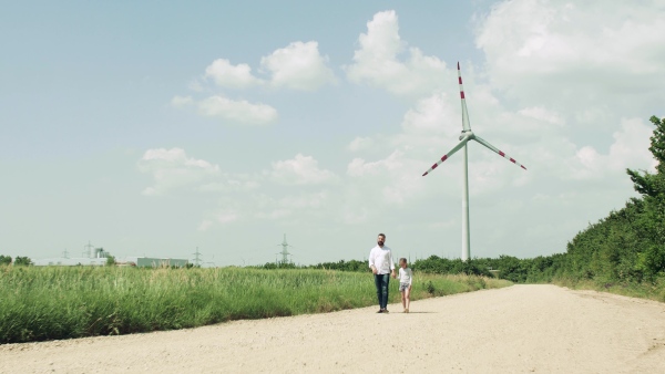 A mature father with small daughter on field on wind farm, walking.