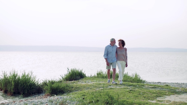 Happy senior couple on a holiday walking by the lake, talking.