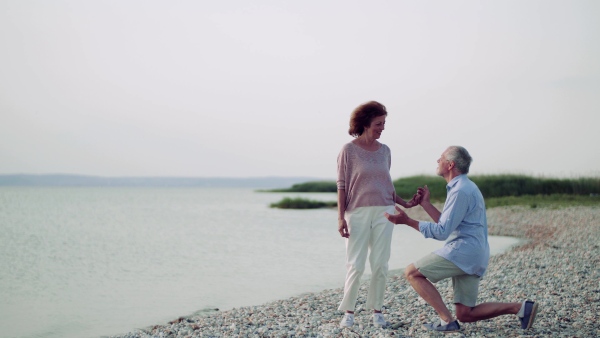 Senior man proposing to a woman on a walk by the lake on holiday.