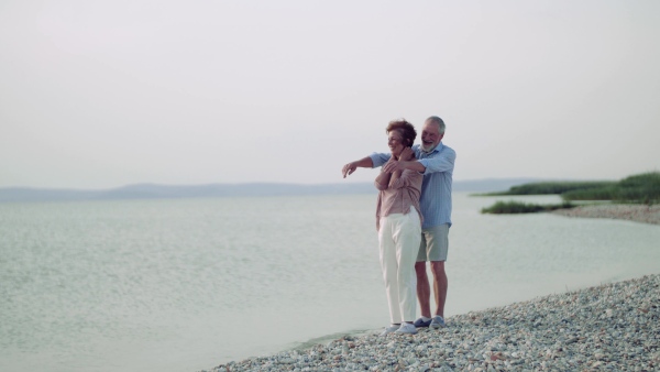 A senior couple on a holiday standing by the lake, hugging.