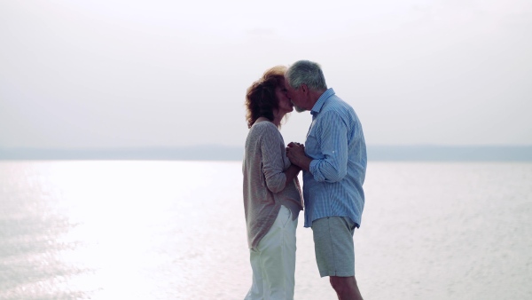 An affectionate senior couple on a holiday on a walk by the lake, kissing.