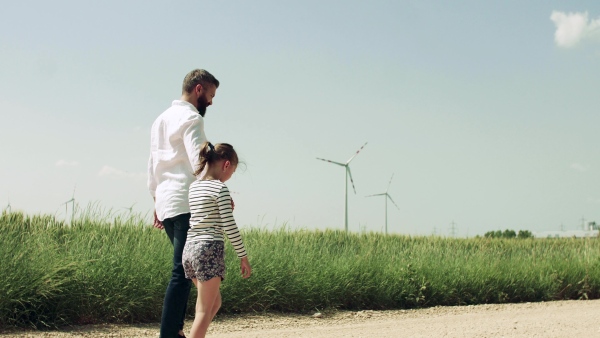 A mature father with small daughter on field on wind farm, walking.