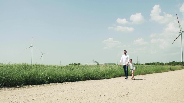 A mature father with small daughter on field on wind farm, walking. Slow motion.