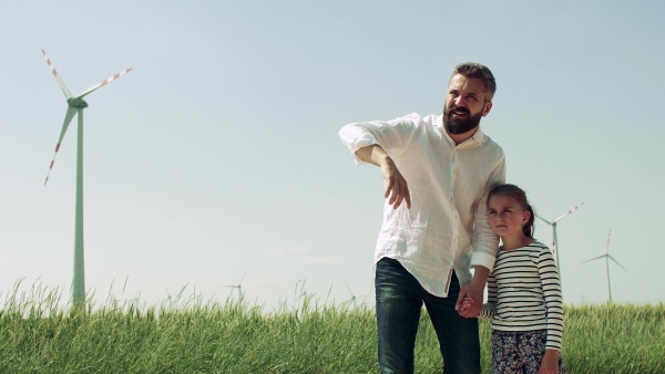 A mature father with small daughter on field on wind farm, talking.