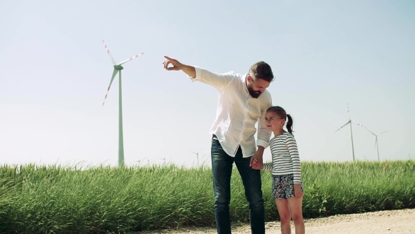 A mature father with small daughter on field on wind farm, talking. Slow motion.