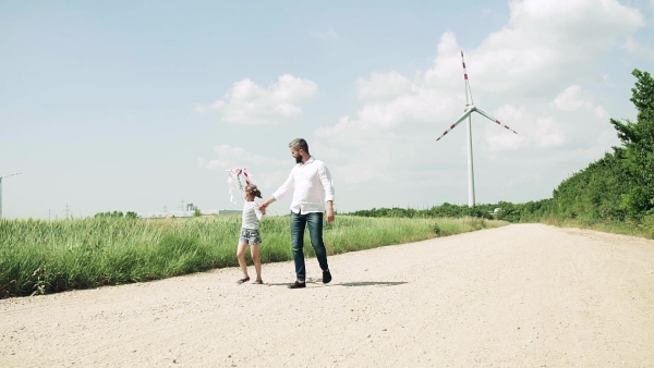 A mature father with small daughter on field on wind farm, walking. Slow motion.