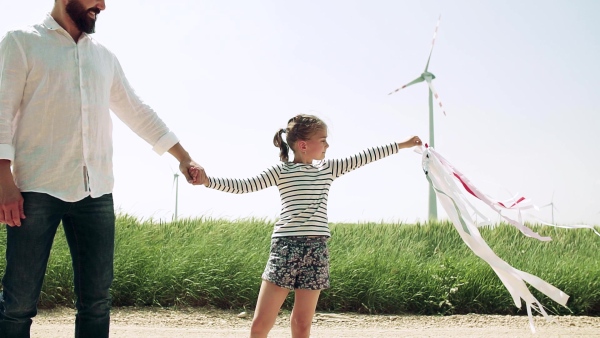 A mature father with small daughter on field on wind farm, playing with hand kite. Slow motion.