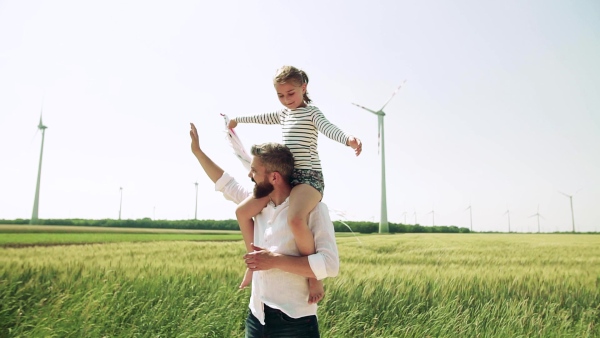 A mature father with small daughter on field on wind farm, playing with hand kite. Slow motion.