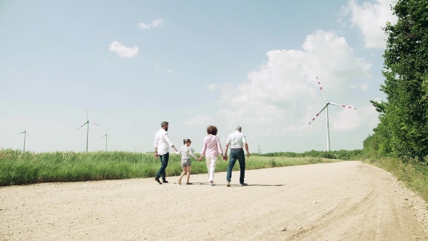 A rear view of multigeneration family walking on field on wind farm. Slow motion.