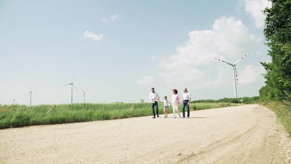 A front view of multigeneration family walking on field on wind farm. Slow motion.