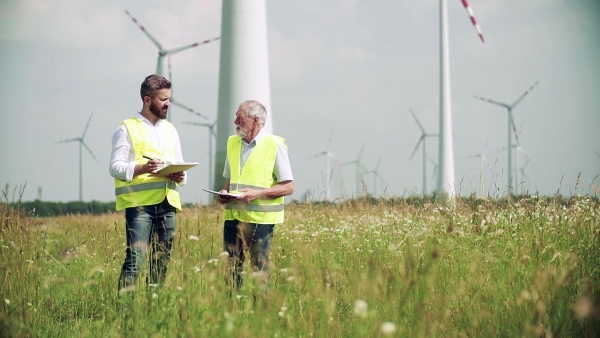 Two engineers or technicians with clipboard standing on wind farm, making notes. Slow motion.