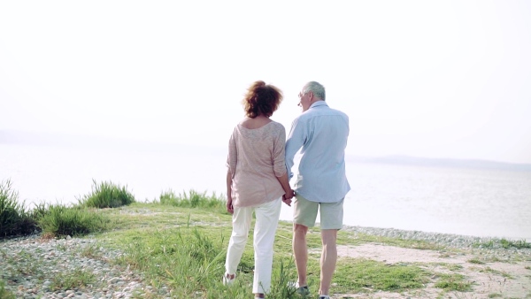 Rear view of senior couple on a holiday on a walk by the lake, walking. Slow motion.