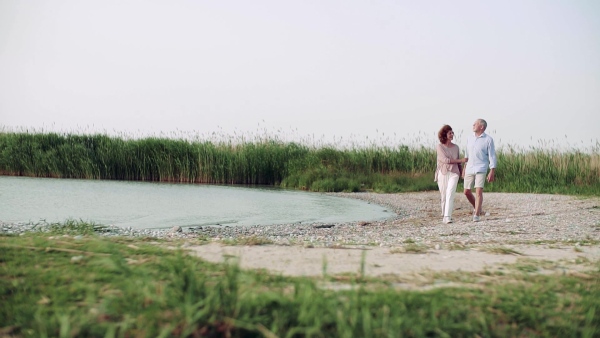 Happy senior couple on a holiday walking by the lake, talking. Slow motion.