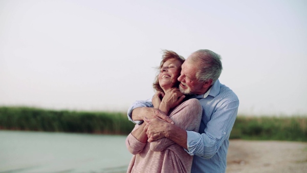 A senior couple on a holiday on a walk by the lake, hugging. Slow motion.