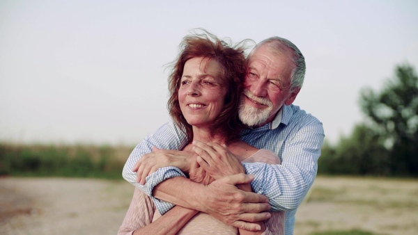 An affectionate senior couple on a holiday standing by the lake, hugging. Slow motion.