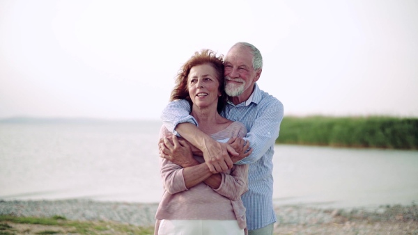 A senior couple on a holiday standing by the lake, hugging. Slow motion.