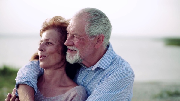 A senior couple on a holiday on a walk by the lake, hugging. Slow motion.