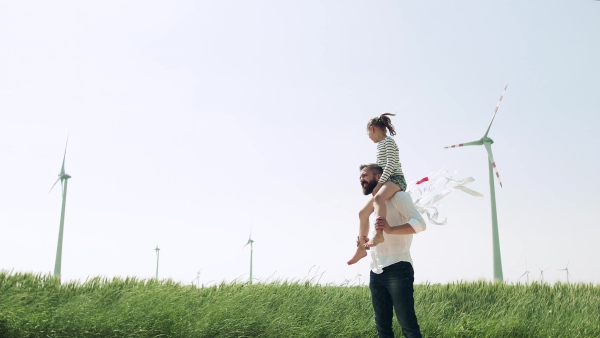 A mature father with small daughter on field on wind farm, playing with hand kite.