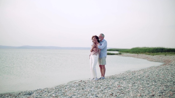 A senior couple on a holiday standing by the lake, hugging. Slow motion.