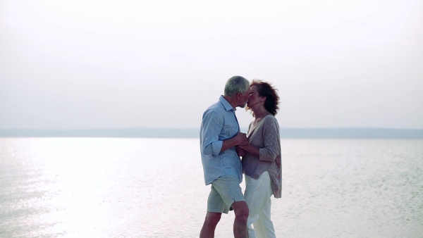 An affectionate senior couple on a holiday on a walk by the lake, kissing. Slow motion.