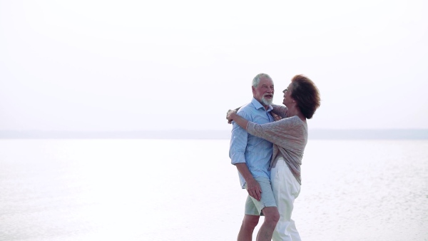 A senior couple on a holiday on a walk by the lake, hugging. Slow motion.