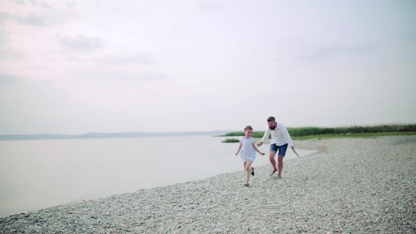 Mature father with small daughter on a holiday by the lake, running. Slow motion.