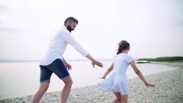 Mature father with small daughter on a holiday by the lake, running. Slow motion.