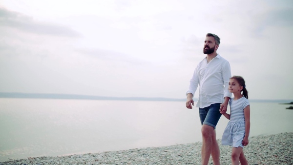 A mature father and small daughter on a holiday walking by the lake or sea. Slow motion.