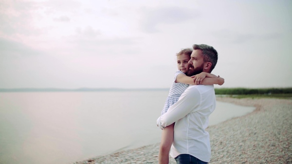 Mature father with small daughter on a holiday standing by the lake, hugging. Slow motion.