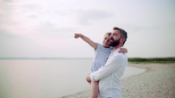 Mature father with small daughter on a holiday standing by the lake, talking. Slow motion.