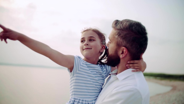 Mature father with small daughter on a holiday standing by the lake, talking. Slow motion.