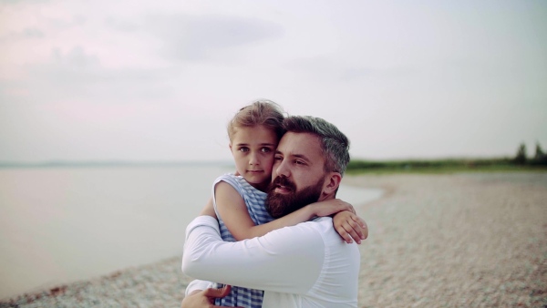 Mature father with small daughter on a holiday standing by the lake, hugging. Slow motion.