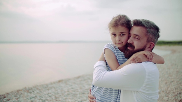 Mature father with small daughter on a holiday standing by the lake, hugging. Slow motion.