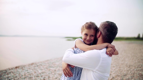 Mature father with small daughter on a holiday standing by the lake, hugging. Slow motion.