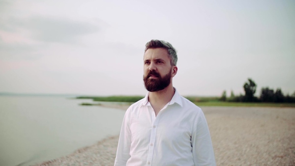 Waist up portrait of mature man on a holiday standing by the lake. Slow motion.