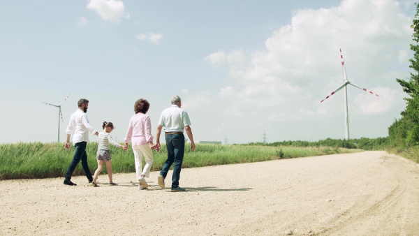 A rear view of multigeneration family walking on field on wind farm.