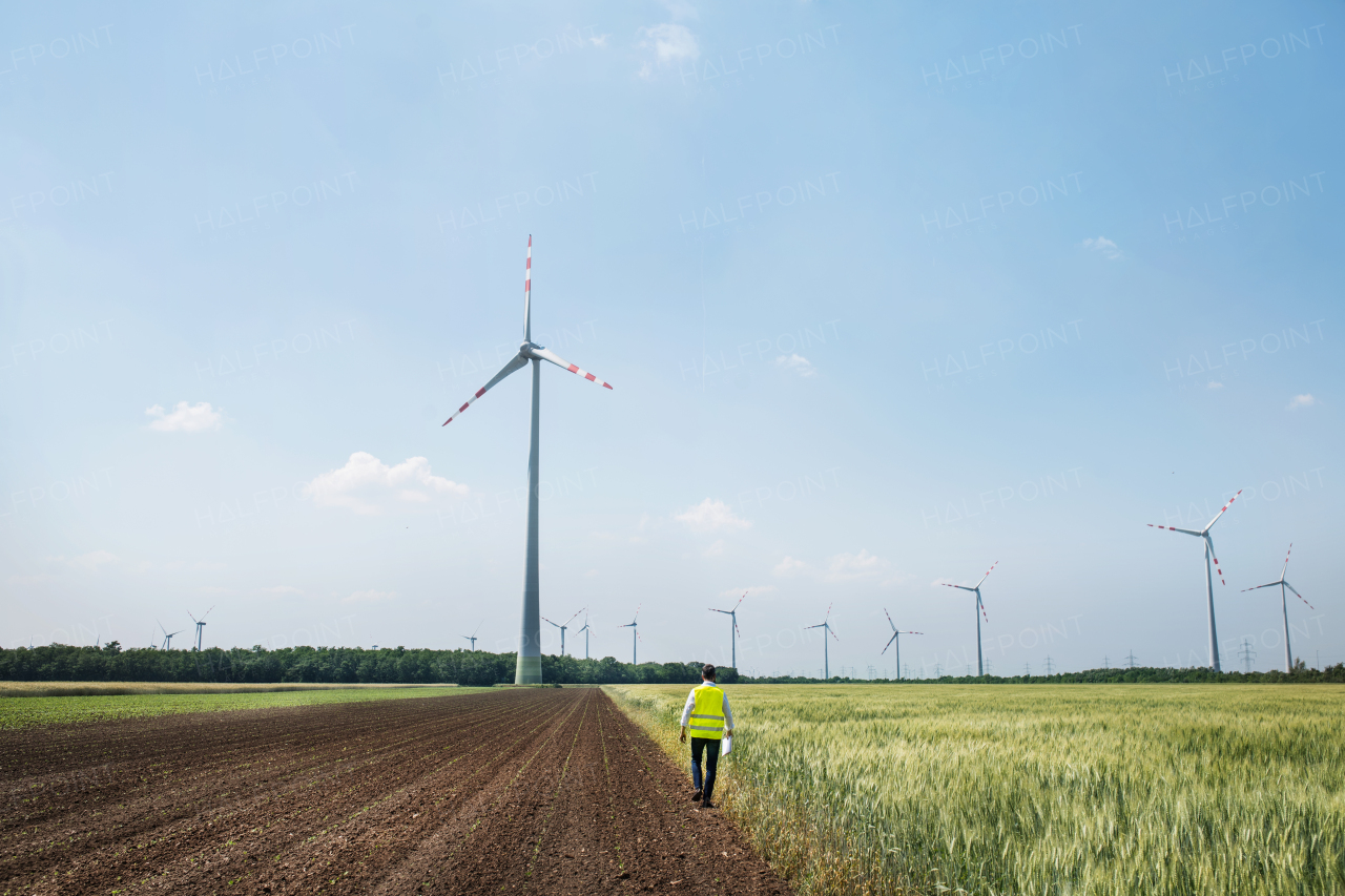 A rear view of an engineer walking on a field on wind farm. Copy space.