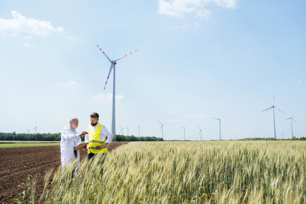 Two engineers or technicians with clipboard standing on wind farm, making notes.