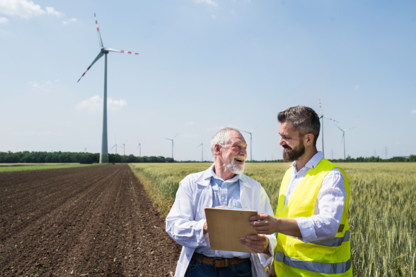 Two engineers or technicians with clipboard standing on wind farm, making notes.