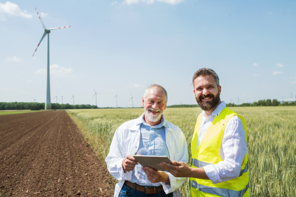 Two engineers or technicians with clipboard standing on wind farm, making notes.