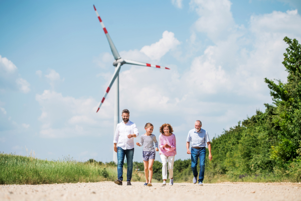 A front view of multigeneration family walking on field on wind farm.