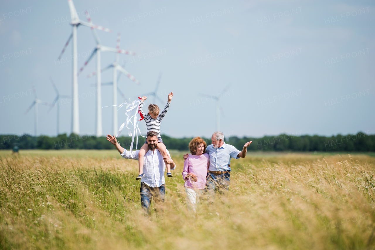 A front view of multigeneration family walking on field on wind farm.